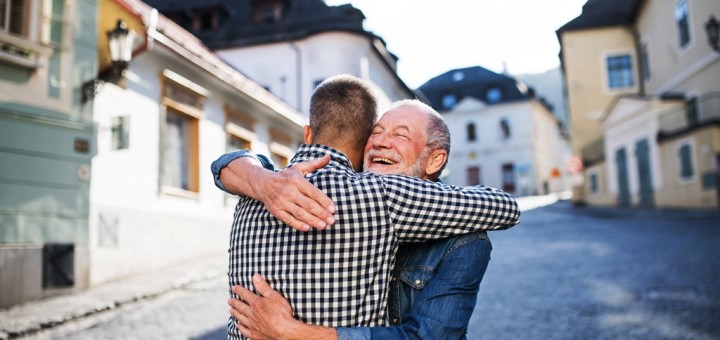 An adult hipster son and his happy senior father in town, hugging.